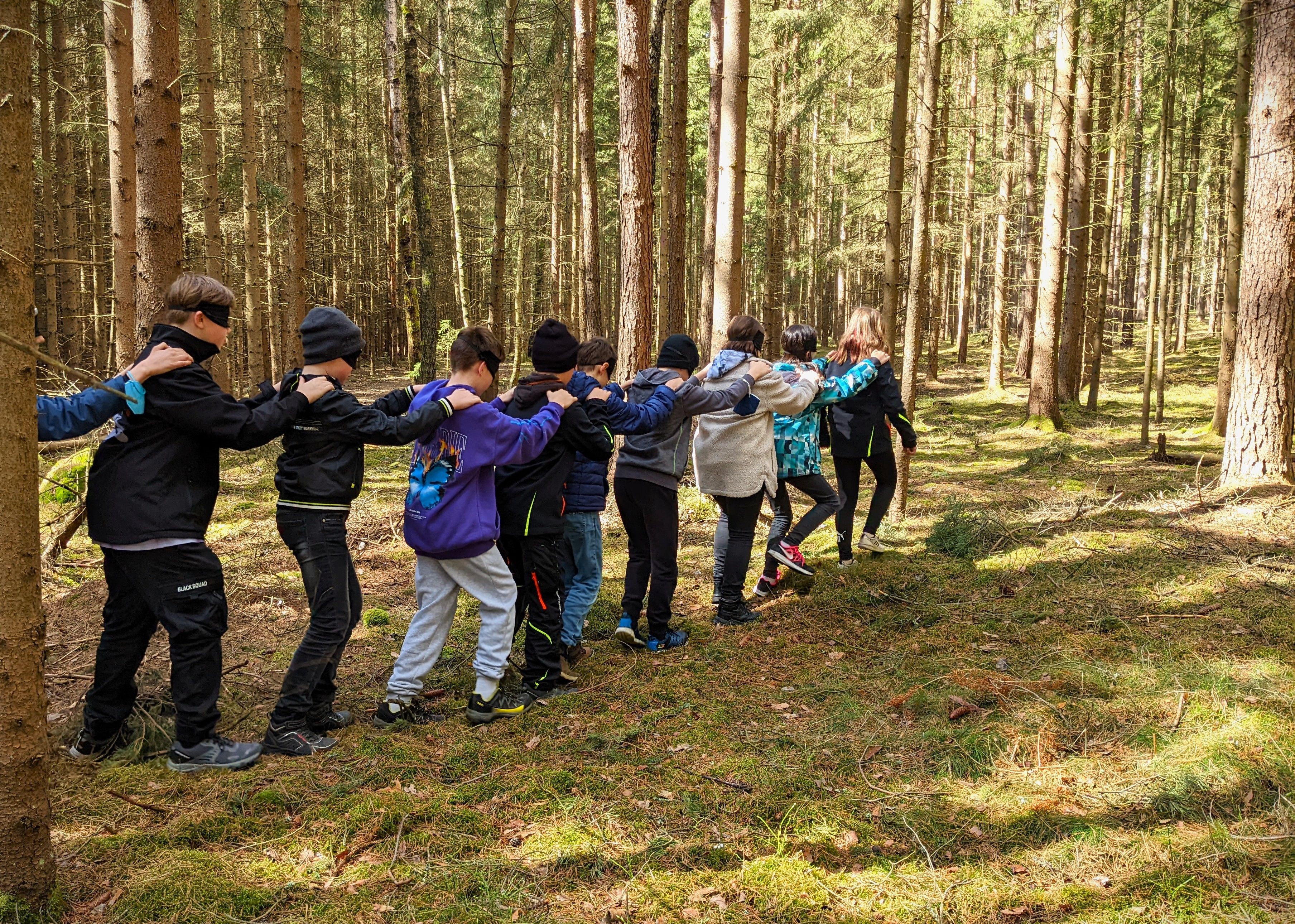 Kinder gehen mit verbundenen Augen durch den Wald und halten sich an den Schultern