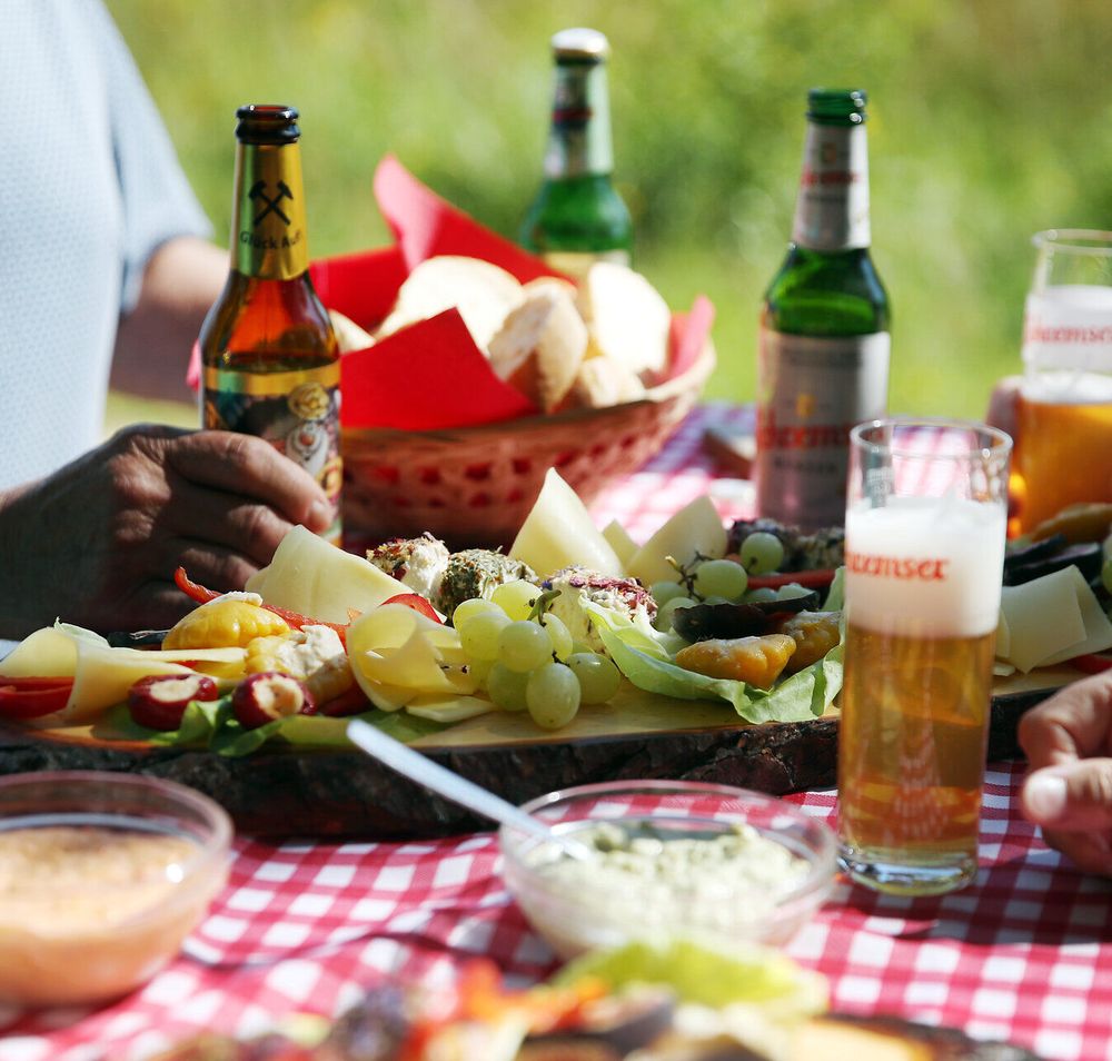 Mehrere Personen sitzen an einem Tisch und genießen Brettljause und Bier. 