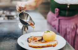 Ein köstlicher Schweinsbraten, perfekt zubereitet und mit einer aromatischen Sauce übergossen, wird auf einem einladenden Teller serviert. Dazu gesellen sich ein traditioneller Waldviertler Knödel und frischer Krautsalat, die die herzliche Wirtshauskultur der Region widerspiegeln. Genießen Sie diese kulinarischen Köstlichkeiten in einer gemütlichen Atmosphäre, die zum Verweilen einlädt.
