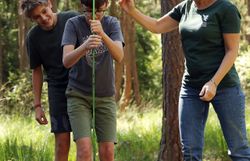Eine Naturvermittlerin lässt einen Jungen mit einer Sonde die Tiefe von einem Moorbecken messen. 