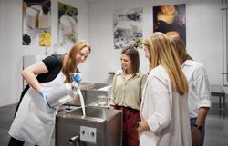 In einer einladenden Atmosphäre erleben Besucher die Kunst der Käseherstellung hautnah. Die Freude und Neugier der Teilnehmer spiegeln sich in ihren Gesichtern wider, während frische Milch in die Maschine gegossen wird. Ein unvergessliches Erlebnis für alle, die die Tradition und den Geschmack regionaler Produkte schätzen.