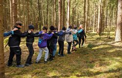 Kinder gehen mit verbundenen Augen durch den Wald und halten sich an den Schultern