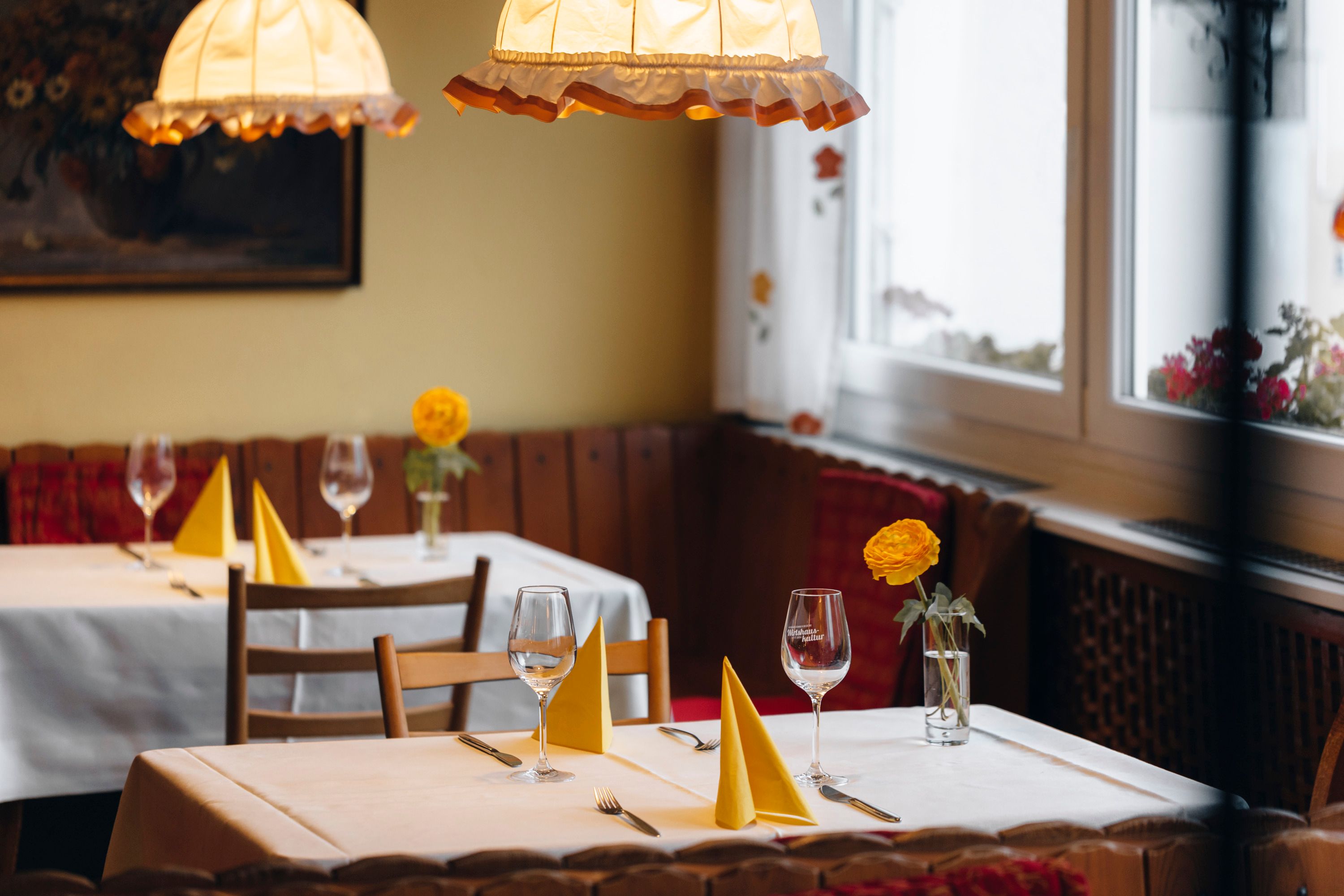 Gemütliches Restaurant mit gedeckten Tischen, gelben Servietten und Blumen.