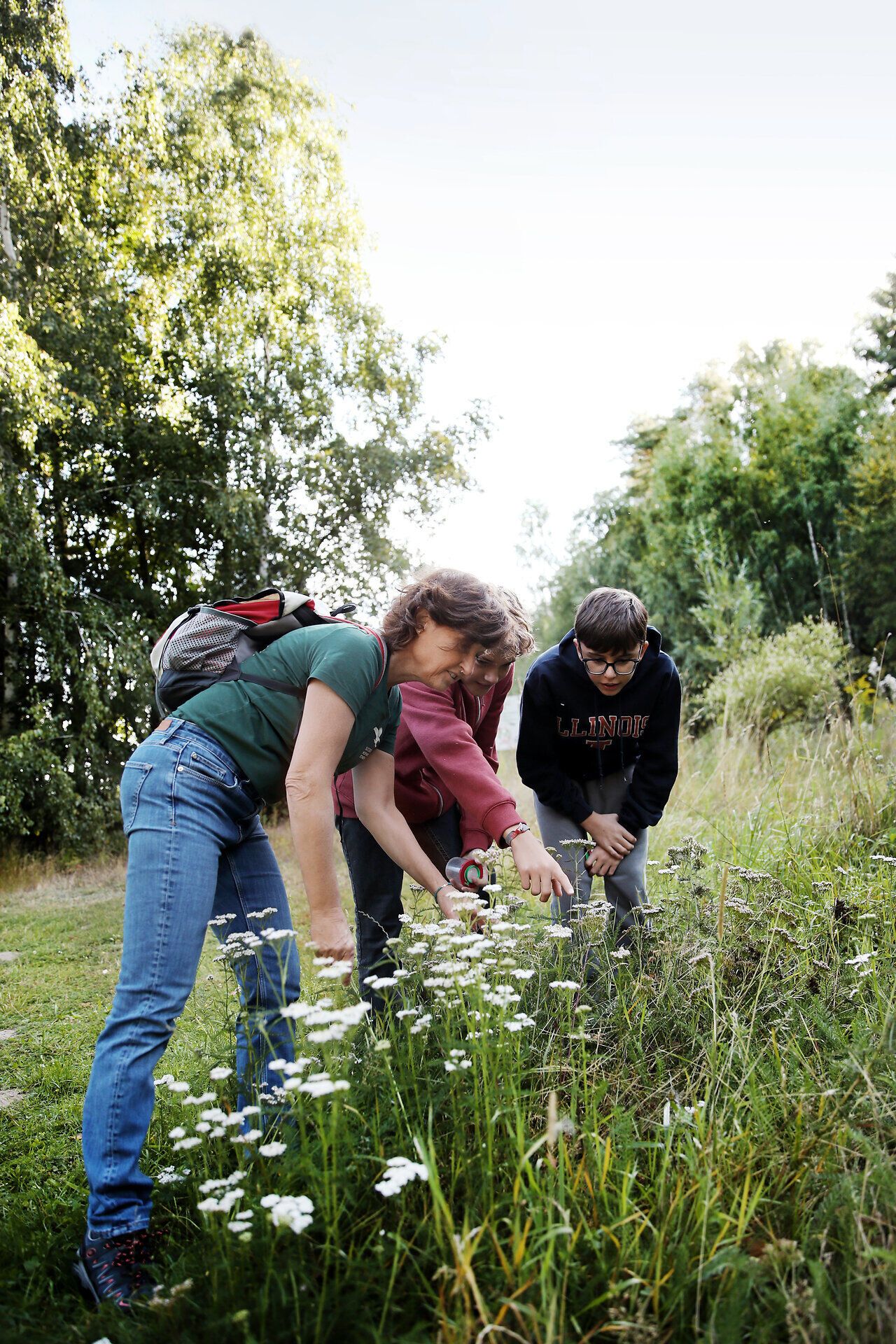 Eine Naturvermittlerin entdeckt gemeinsam mit zwei Jugendlichen die Vegetation am Wegesrand. 
