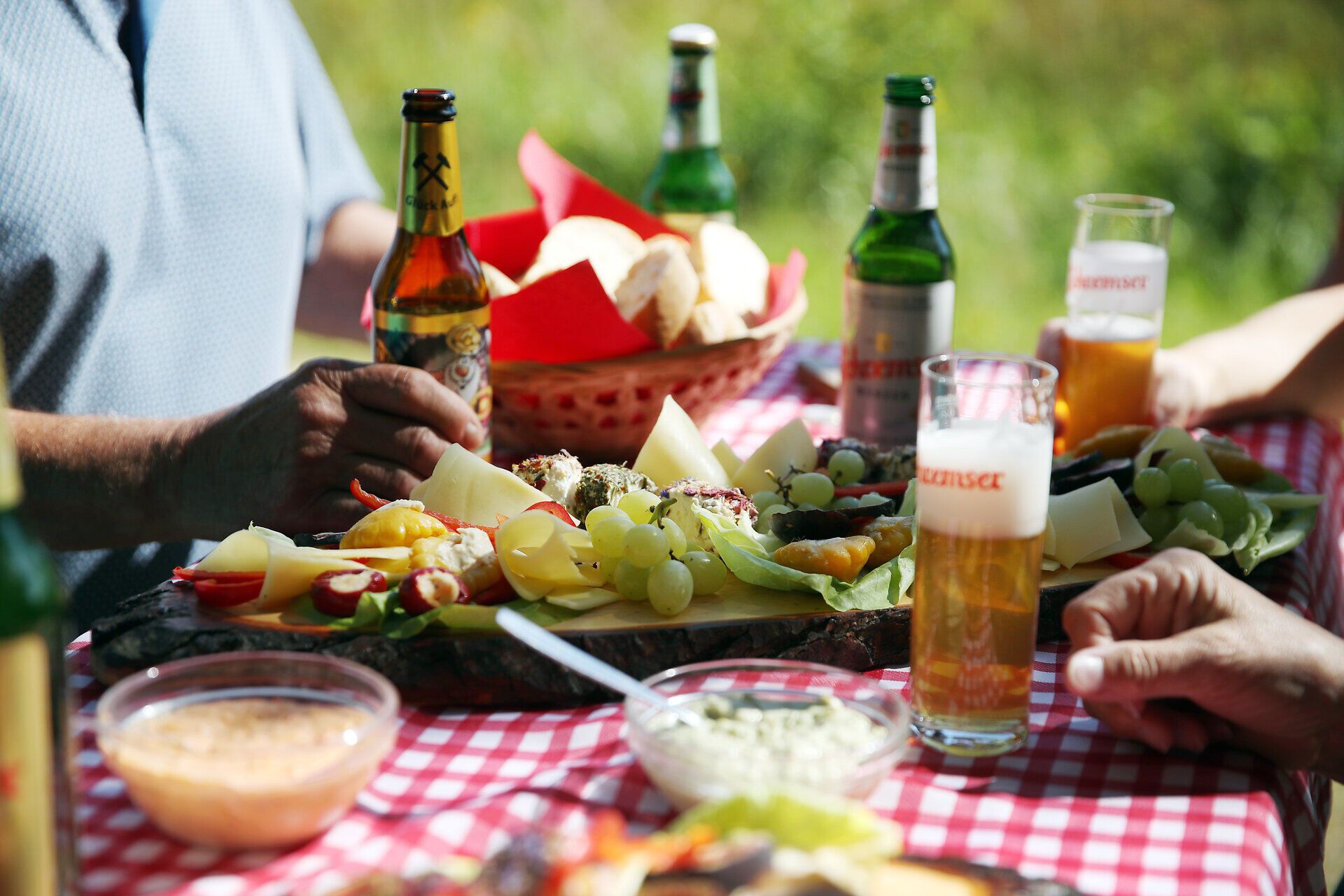 Mehrere Personen sitzen an einem Tisch und genießen Brettljause und Bier. 