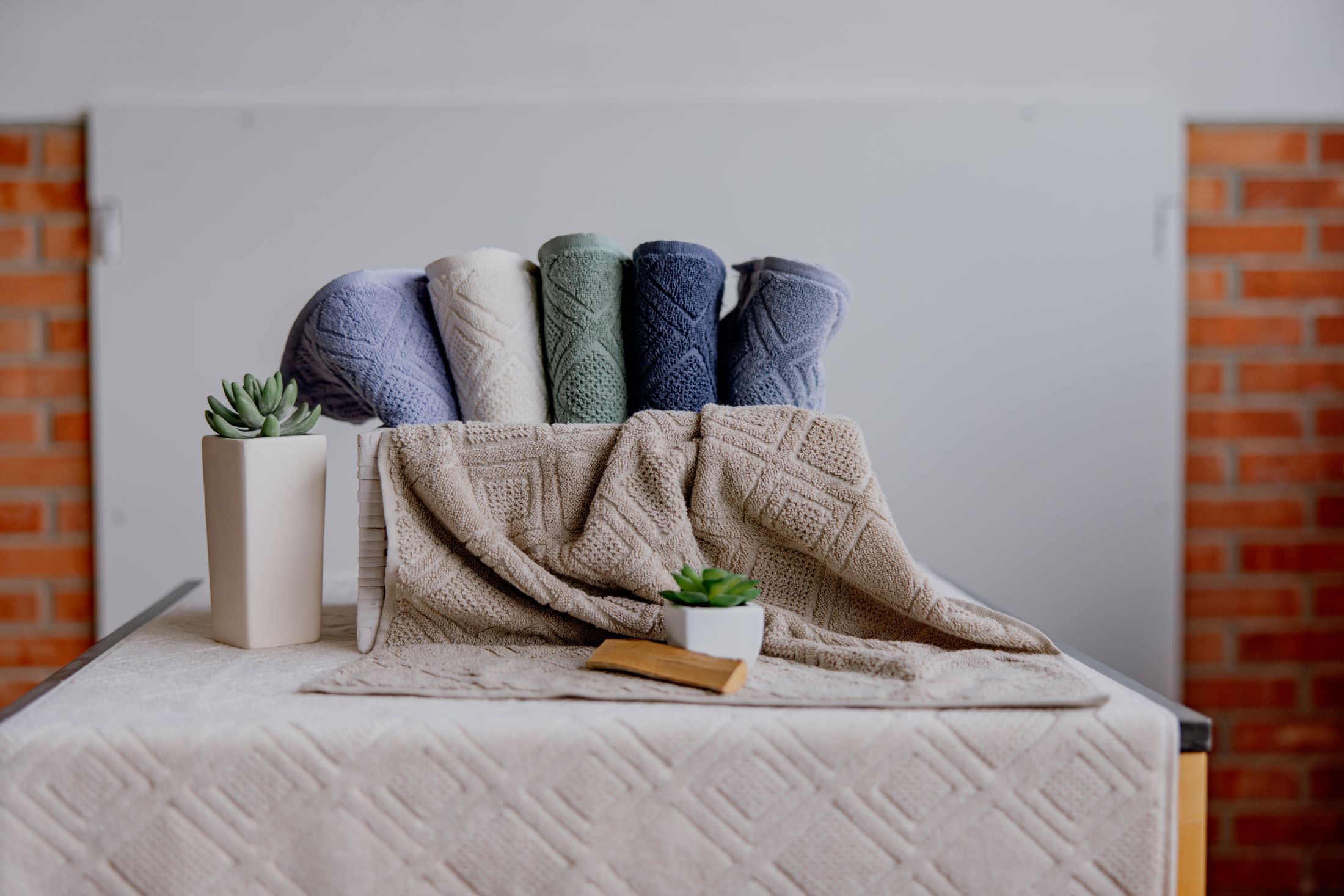 Farbige Handtücher und Pflanzen auf einem Tisch vor einer Ziegelwand.