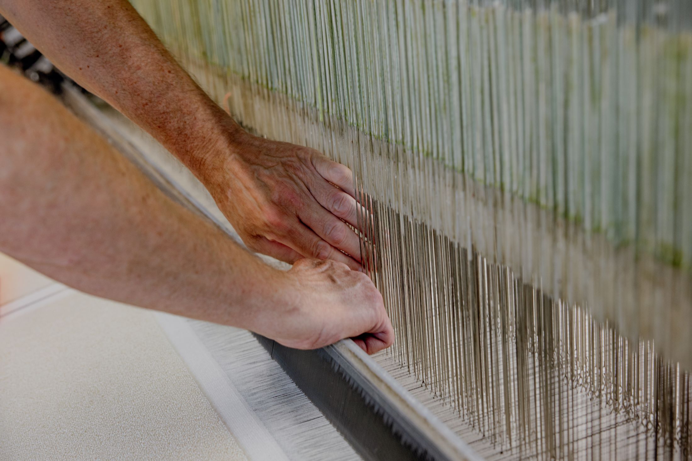 Nahaufnahme von Händen, die an einem Webstuhl arbeiten.
