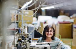 In der warmen, einladenden Atmosphäre der Textilwerkstatt wird mit Geschick und Leidenschaft an hochwertigen Frottierwaren gearbeitet. Die sanften Geräusche der Nähmaschinen und das Spiel von Licht und Schatten schaffen eine harmonische Umgebung, die die Kreativität und Handwerkskunst widerspiegelt.