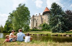 Die malerische Burg Heidenreichstein thront majestätisch über dem ruhigen Gewässer, während eine Familie entspannt im Gras sitzt und die Schönheit der Natur genießt. Umgeben von üppigem Grün und hohen Bäumen, strahlt der Ort eine friedliche Atmosphäre aus, die zum Verweilen einlädt.