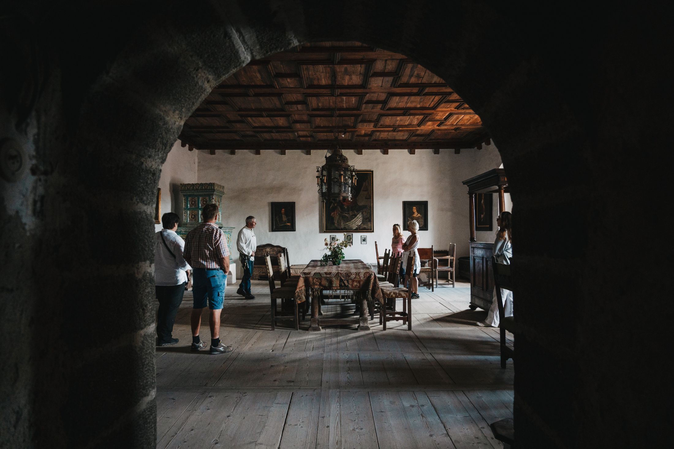 Innenansicht eines historischen Raumes mit Besuchern, Holzmöbeln und Gemälden an den Wänden.