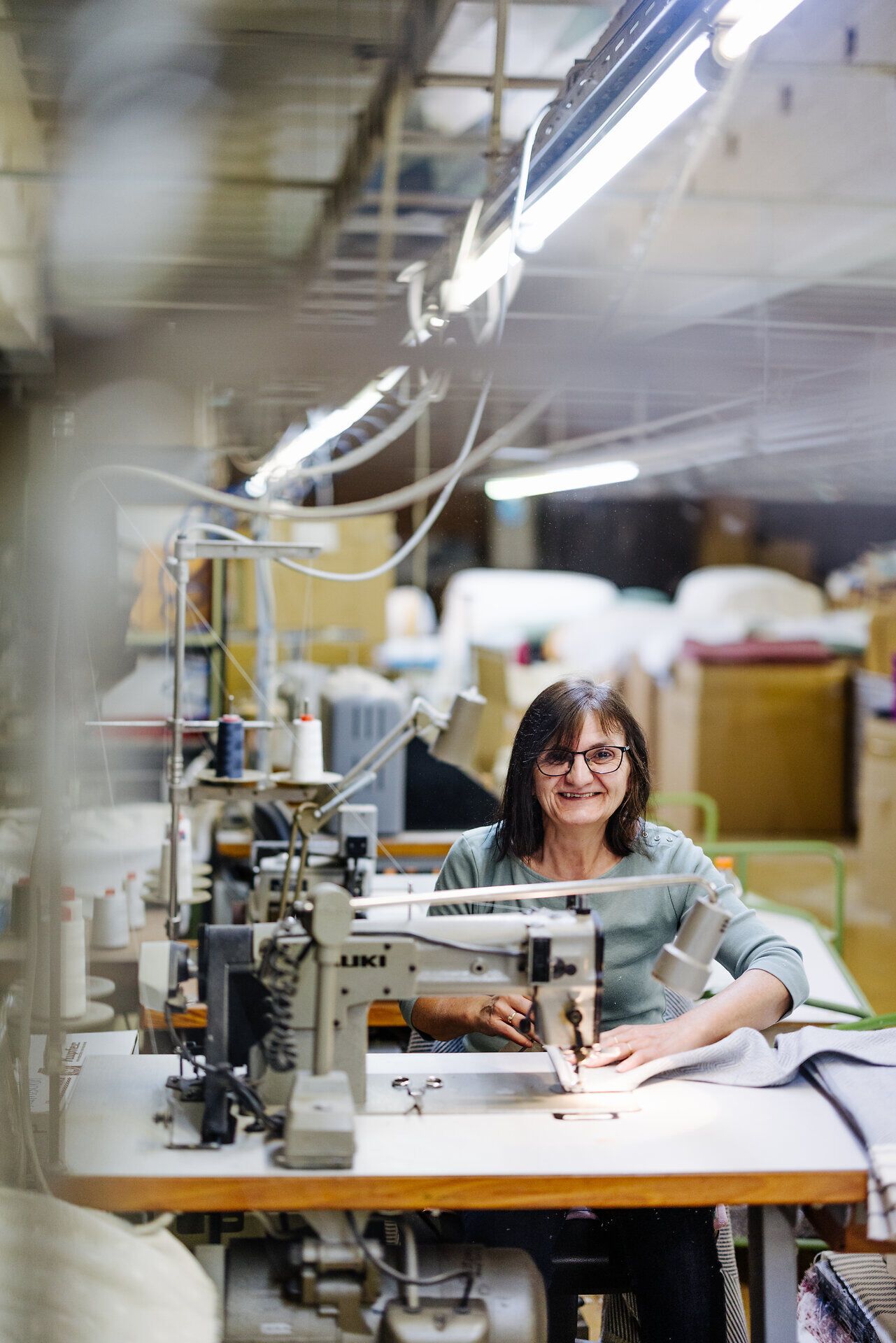 In der warmen, einladenden Atmosphäre der Textilwerkstatt wird mit Geschick und Leidenschaft an hochwertigen Frottierwaren gearbeitet. Die sanften Geräusche der Nähmaschinen und das Spiel von Licht und Schatten schaffen eine harmonische Umgebung, die die Kreativität und Handwerkskunst widerspiegelt.
