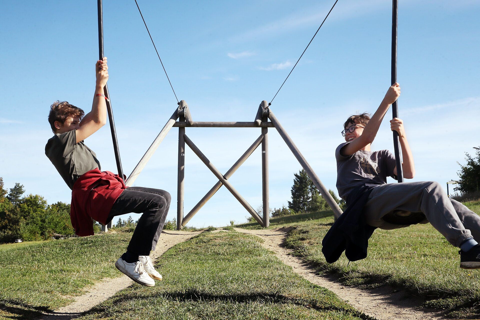 Zwei Burschen fahren mit der Doppel-Seilbahn am Spielplatz im Naturpark Heidenreichstein. 
