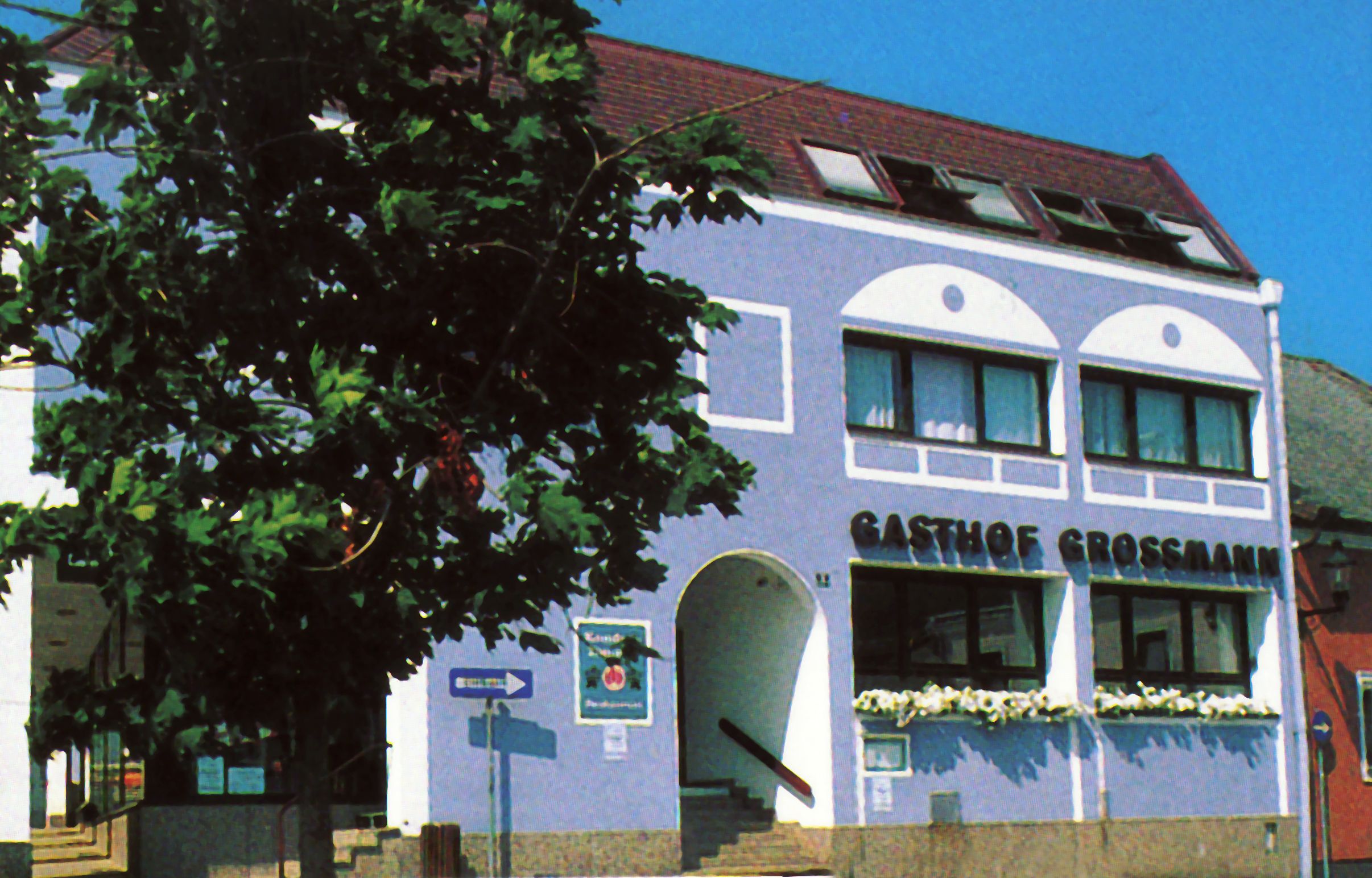 Gasthof Großmann mit blauer Fassade und Baum im Vordergrund.